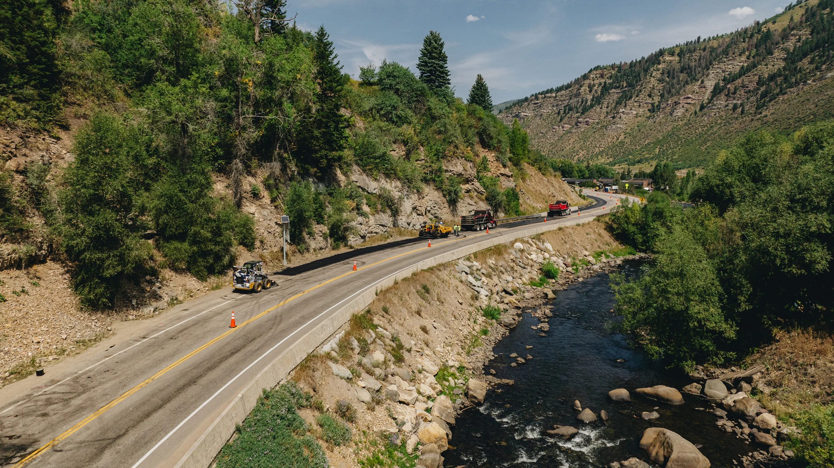 Aerial view of MD Asphalt paving a Colorado mountain road beside a river